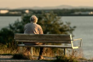 Serene scene of a senior man sitting on a bench by a lake during sunset.