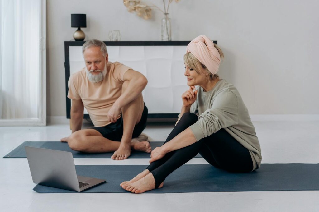 Elderly couple practicing yoga online at home, promoting wellness.