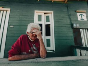 Pensive elderly woman sitting on a porch, evoking feelings of reflection and solitude.