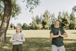 Elderly couple meditating in a calm park setting, embracing fitness and tranquility outdoors.