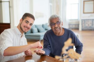 Smiling young man and senior man bonding indoors at a wooden table.