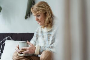Elderly woman sitting thoughtfully with a coffee cup, indoors, relaxed setting.