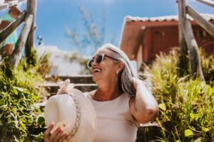 Happy senior woman with sunglasses and sunhat smiling outdoors on a sunny day.