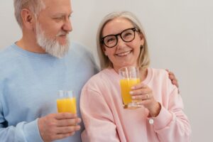 Smiling elderly couple holding glasses of fresh orange juice indoors.