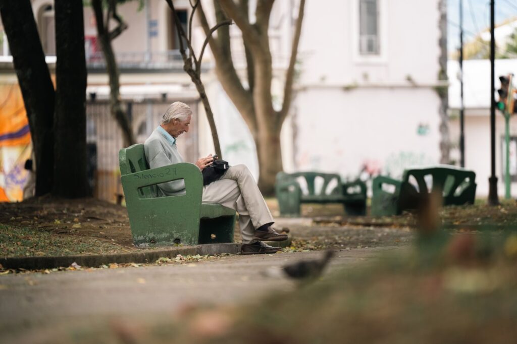 An elderly man sits quietly on a park bench in San José, Costa Rica, enjoying a peaceful day outdoors.