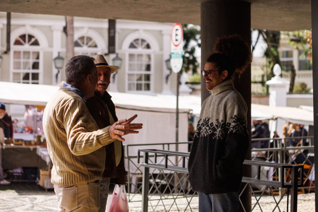 Three men casually chatting in an outdoor market in Curitiba, Brazil, captured during a sunny day.
