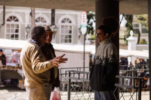 Three men casually chatting in an outdoor market in Curitiba, Brazil, captured during a sunny day.