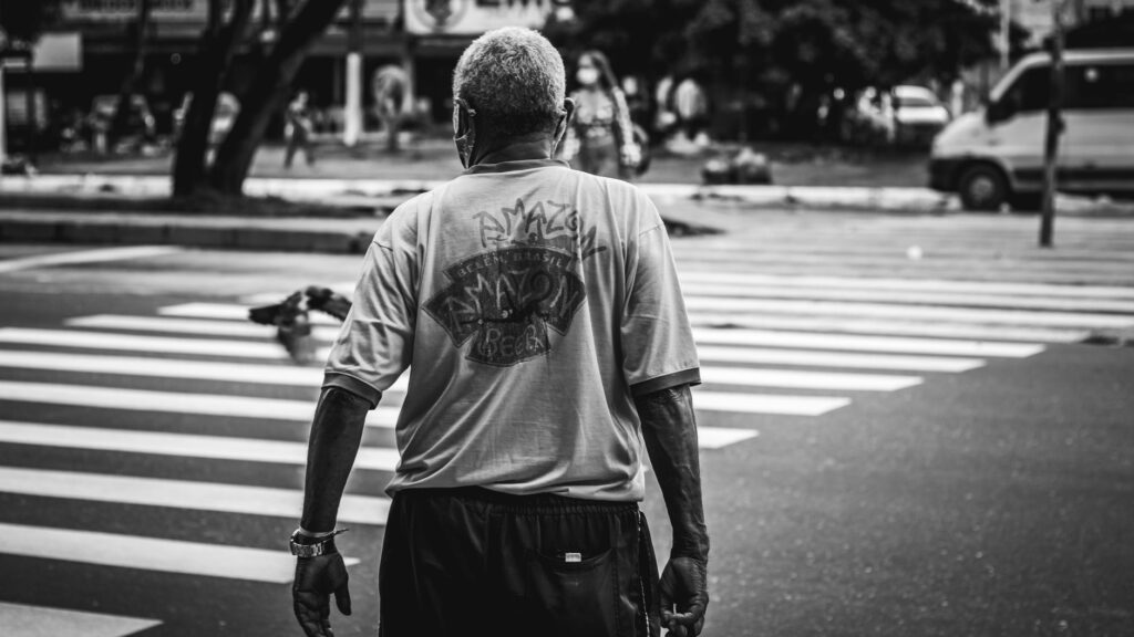 Black and white image of a man crossing a pedestrian lane in an urban setting.