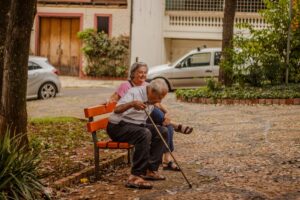 Senior couple enjoying a peaceful moment on a park bench in an urban setting with cars and greenery.