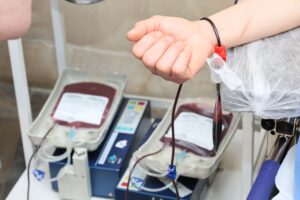 Close-up of blood donation process showing a donor's arm and blood bags in a clinic.