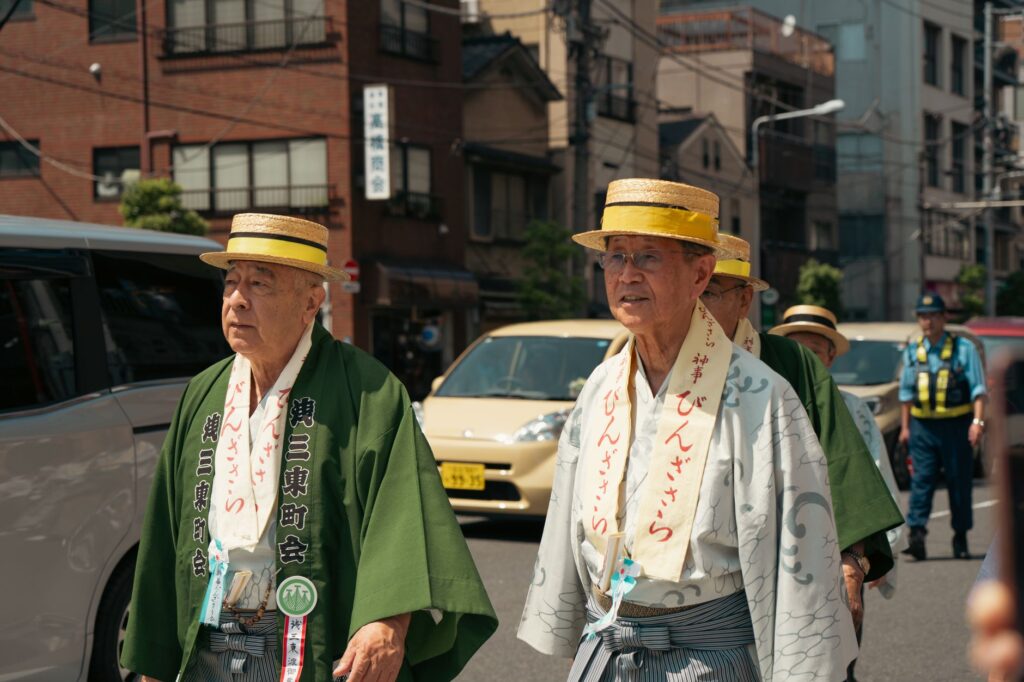Elderly men in traditional attire participate in a cultural parade during a sunny day in Tokyo.