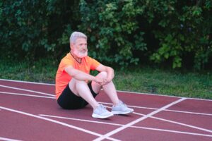 Side view of aged gray haired male in activewear looking away sitting on stadium track while having rest