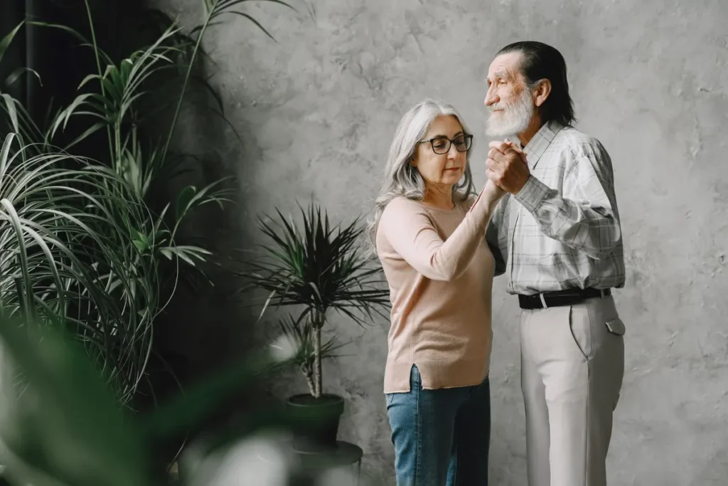 Joyful elderly couple dancing together in a cozy indoor garden, celebrating love and companionship.