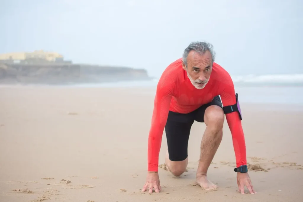 Elderly man in activewear ready to jog on a scenic beach in Portugal.