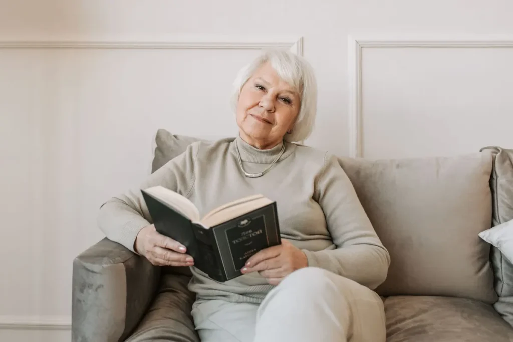 Senior woman with white hair enjoys a book while sitting on a comfortable sofa indoors.