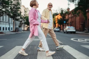 Happy senior couple holding hands and walking across a pedestrian crossing in an urban street.