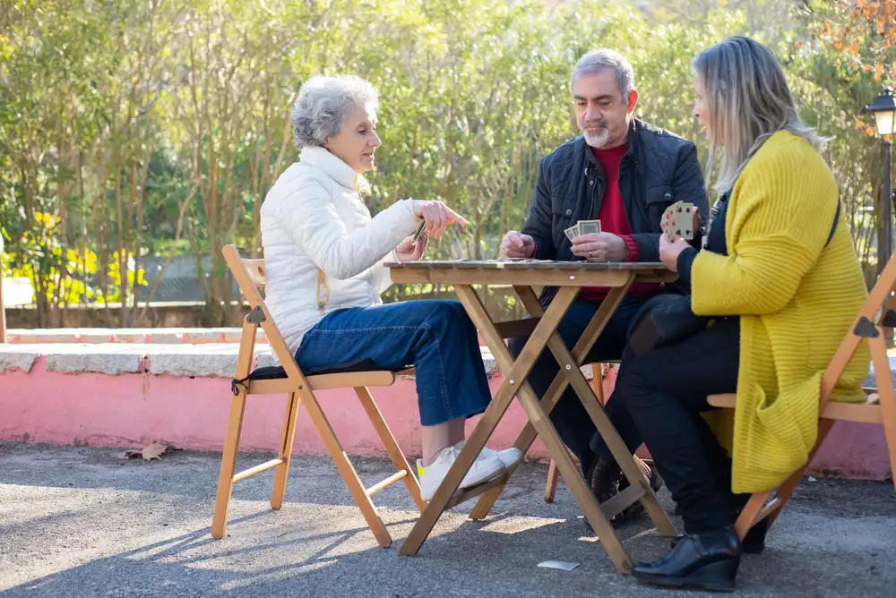 Three senior friends playing a card game outdoors, enjoying leisure time together.