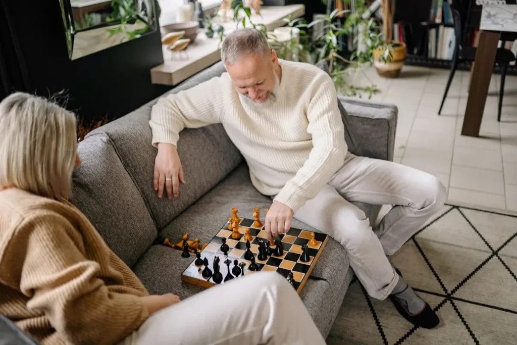 A senior couple playing chess on a cozy sofa, embracing leisure and strategy indoors.