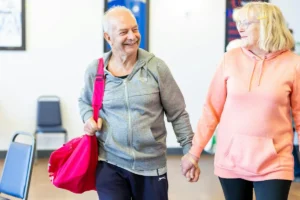Happy senior couple holding hands and smiling in a gym setting, wearing casual sports clothing.