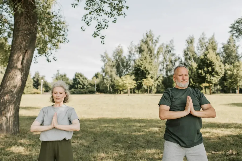 Elderly couple meditating in a calm park setting, embracing fitness and tranquility outdoors.