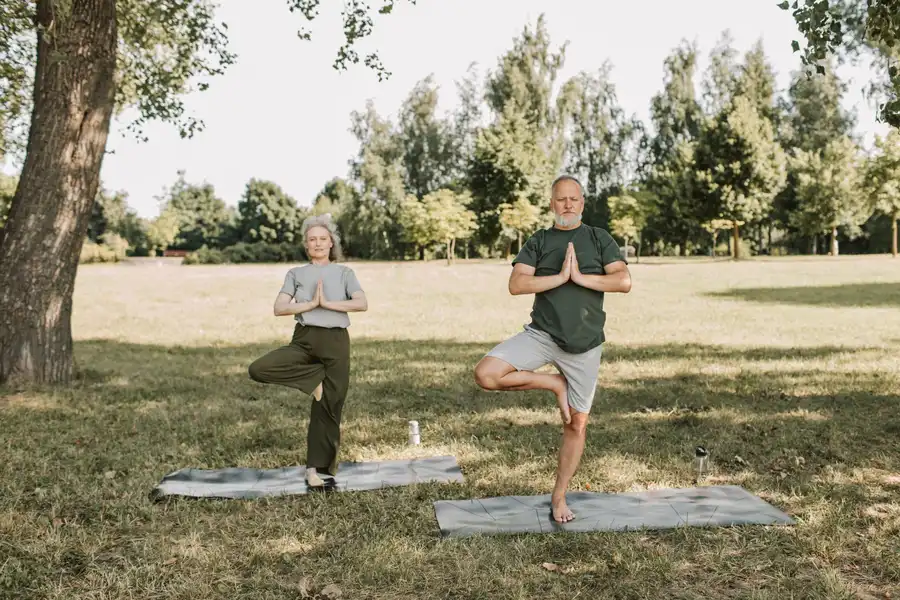 An elderly couple doing yoga in a serene park setting, promoting a healthy lifestyle.