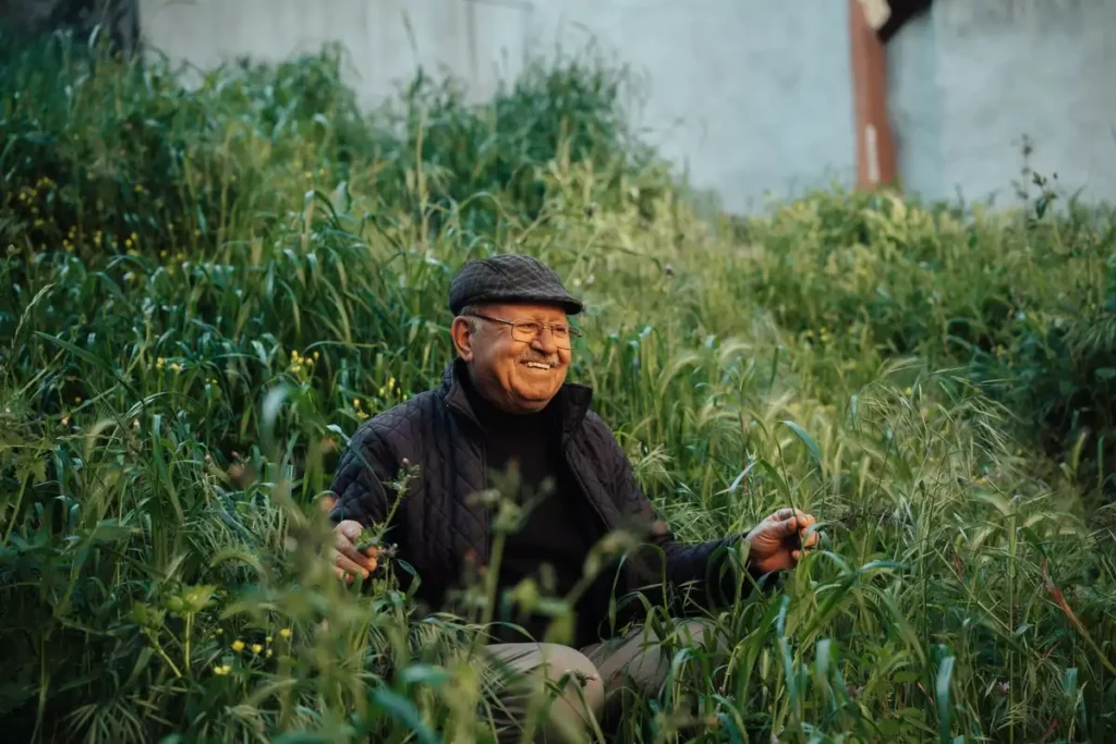 A senior man sitting happily in lush grass in an İstanbul park, enjoying nature.
