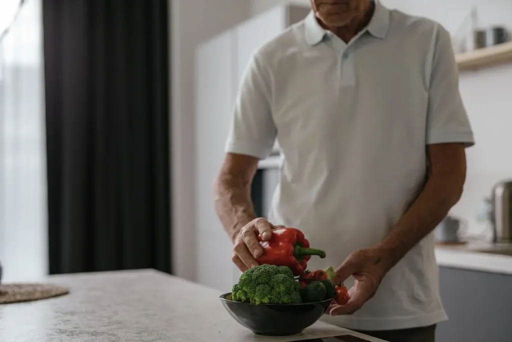 Elderly man in kitchen holding vegetables, embracing a healthy lifestyle.