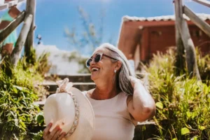 Happy senior woman with sunglasses and sunhat smiling outdoors on a sunny day.