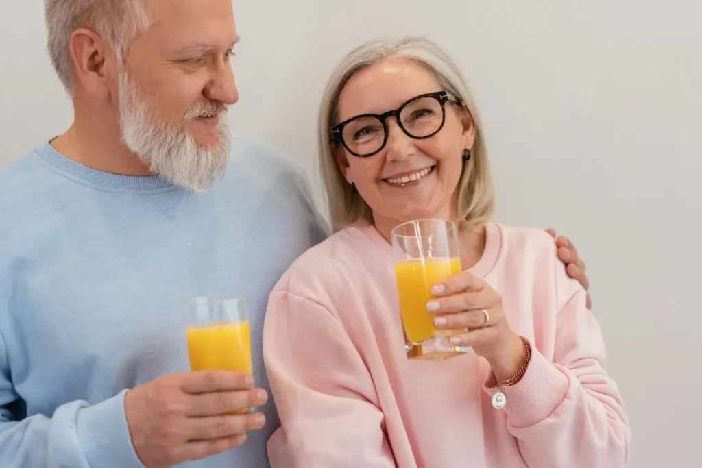 Smiling elderly couple holding glasses of fresh orange juice indoors.