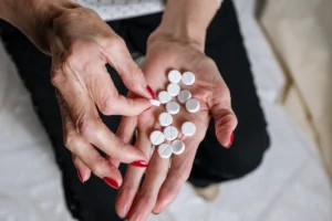 Senior woman's hands with red nails holding circular white tablets, depicting medication concept.
