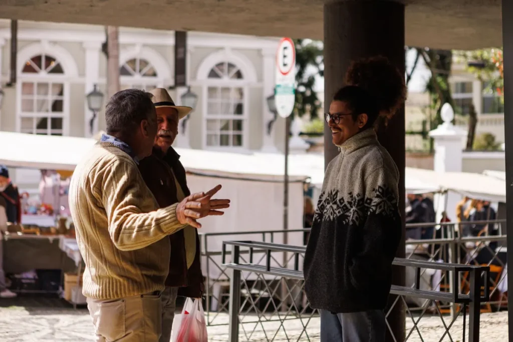 Three men casually chatting in an outdoor market in Curitiba, Brazil, captured during a sunny day.