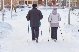 Elderly couple enjoying a winter walk with ski poles in a snowy park setting.