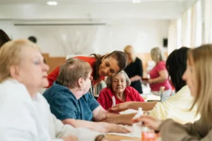 Smiling caregivers and seniors engage over a table at a community center.