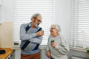 Senior couple smiling and enjoying green smoothies in a cozy kitchen setting.