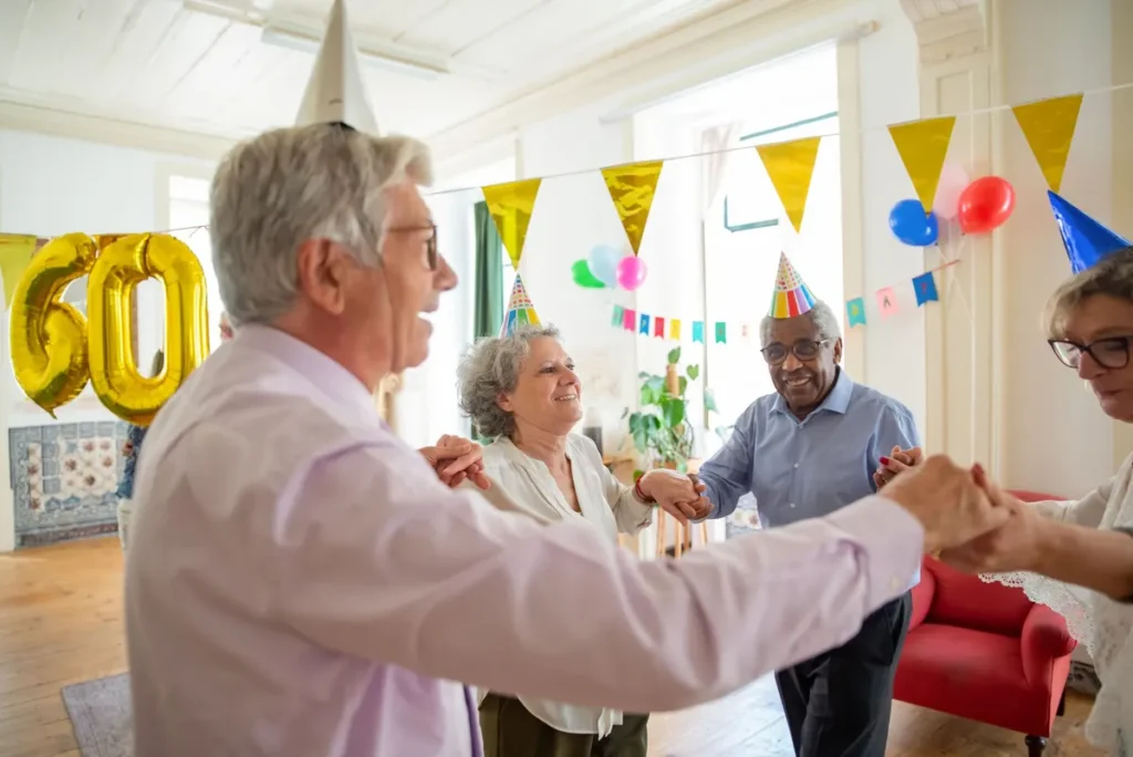 Group of seniors celebrating a birthday indoors with party hats and decorations.