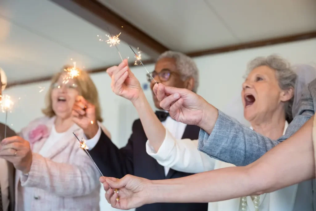 Elderly friends joyfully celebrate indoors holding sparklers. Embracing togetherness and fun.