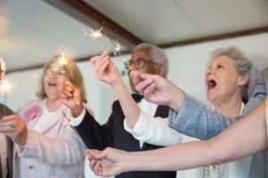 Elderly friends joyfully celebrate indoors holding sparklers. Embracing togetherness and fun.