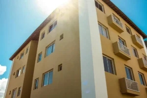 A newly constructed modern apartment building with balconies and windows under bright sunlight.