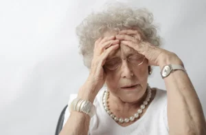 An elderly woman with her hands on her head, appearing stressed or in pain.