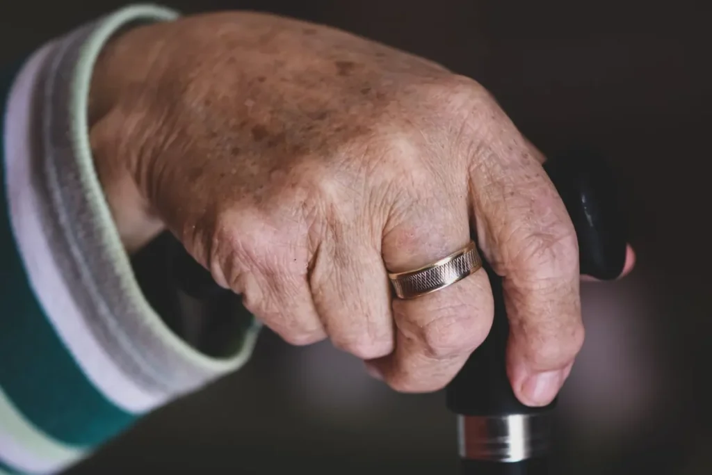 Detailed view of a senior adult's hand holding a cane, wearing a silver ring.