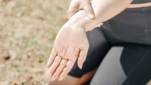 Person gripping wrist in pain, highlighting injury and support outdoors.